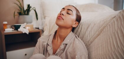 Woman experiencing allergy fatigue resting in bed with medication on nightstand